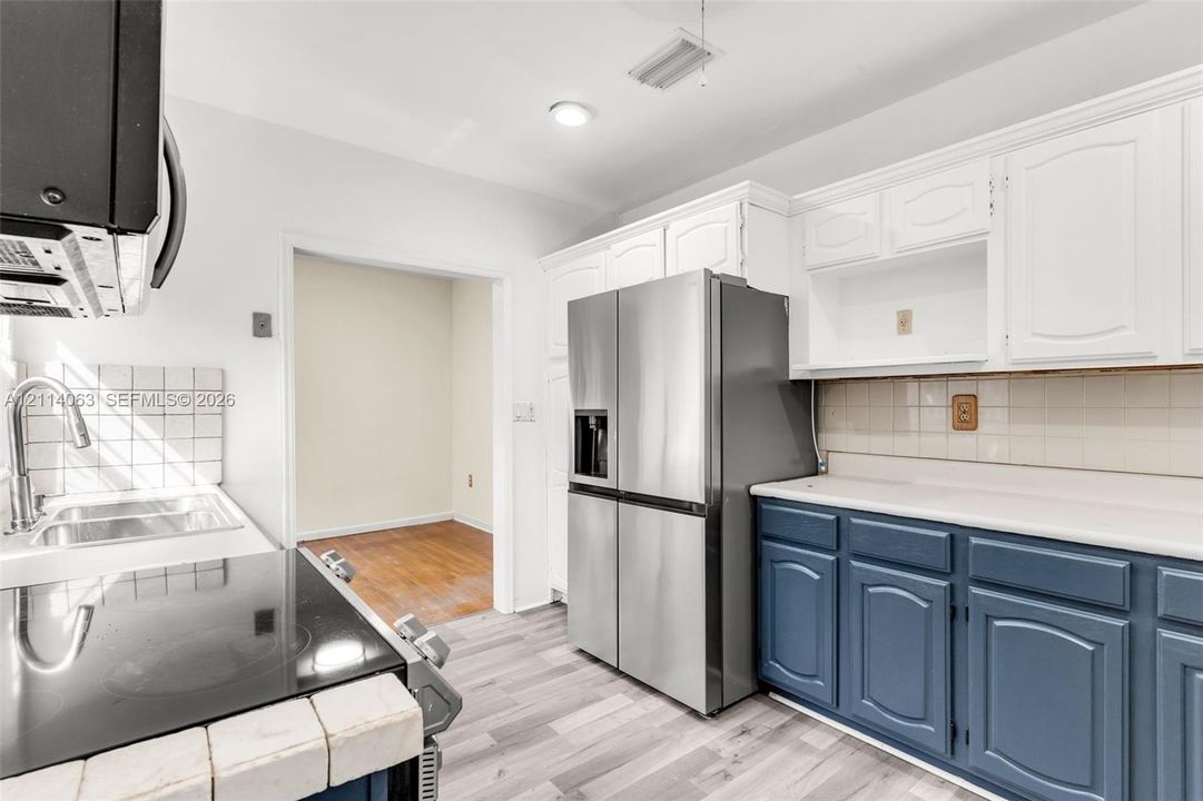 Kitchen featuring stainless steel refrigerator, white upper cabinetry, blue lower cabinetry, ceramic tile backsplash, and wood-finish flooring