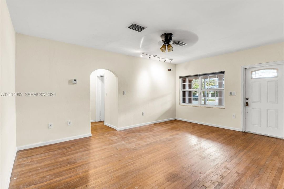 Living area featuring wood-finish flooring, an arched entryway, multi-pane window, ceiling fan with integrated lighting, and a paneled entry door with a transom window