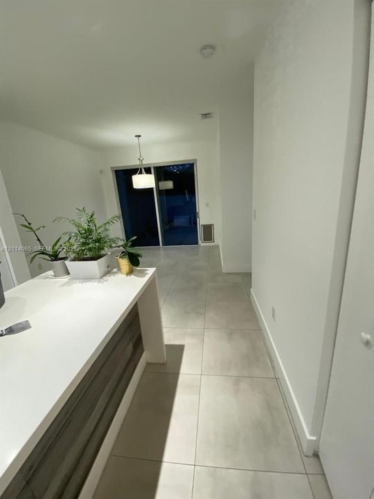 Kitchen island featuring a solid white countertop and wood-finish cabinetry, complemented by large-format tile flooring, a hanging pendant light fixture, and sliding glass doors