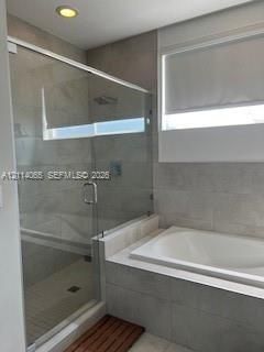 Walk-in glass enclosed shower with a rain-style showerhead, tiled-in soaking tub, large-format wall tiling, and recessed ceiling lighting