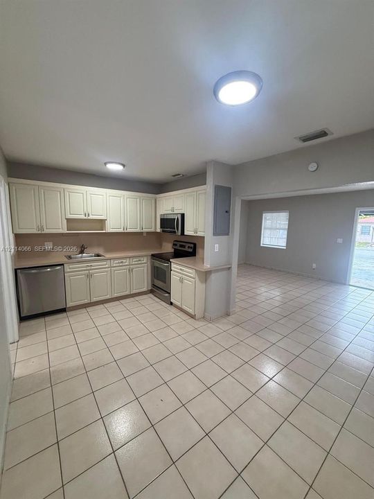 Kitchen featuring off-white cabinetry, stainless steel appliances, neutral tile flooring, and flush-mount ceiling lighting
