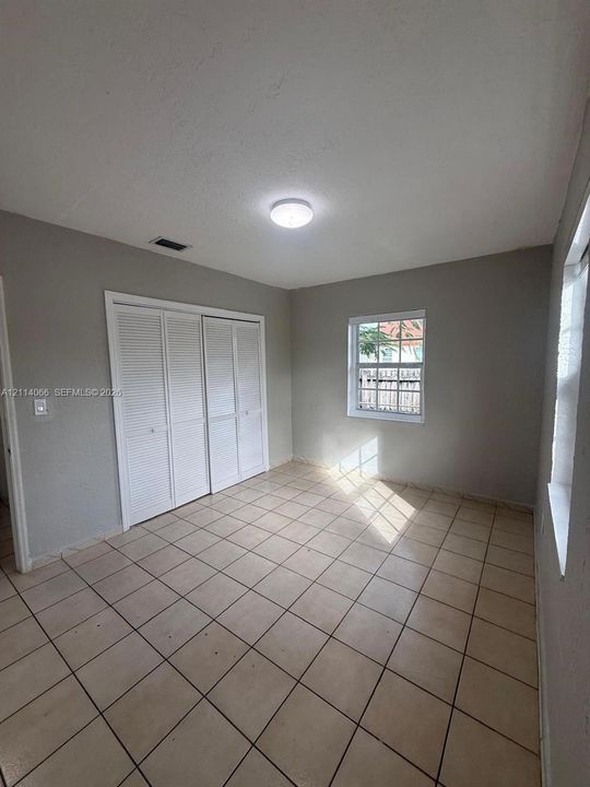 Neutral-toned interior featuring ceramic tile flooring, built-in closet with louvered doors, and multi-pane windows