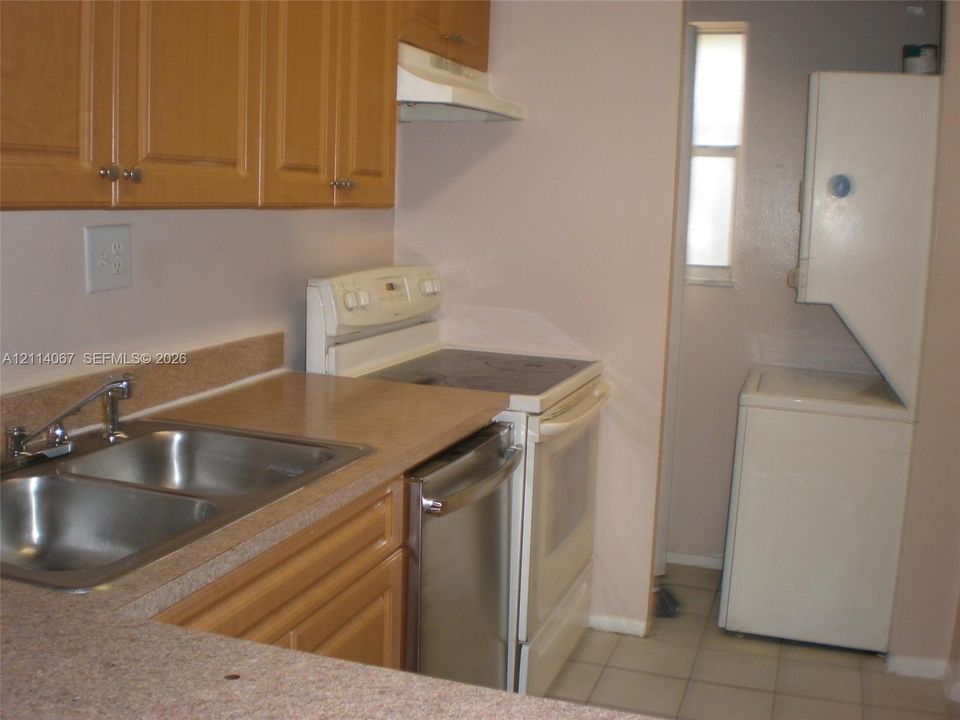 Kitchen featuring wood cabinetry, stainless steel double-basin sink, laminate countertops, integrated range, and an in-unit stacked laundry appliance