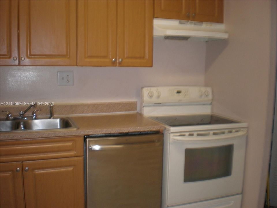 Kitchen featuring wood-finish cabinetry, stainless steel dishwasher, white range with glass cooktop, dual-basin stainless steel sink, and integrated range hood