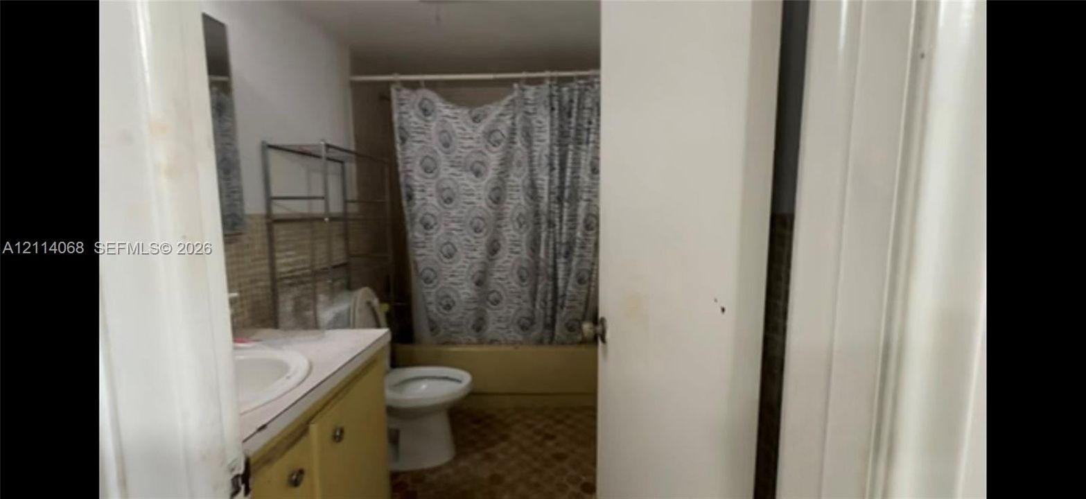 Bathroom featuring a vanity with a white countertop and integrated sink, a porcelain toilet, and a bathtub with tiled surround walls