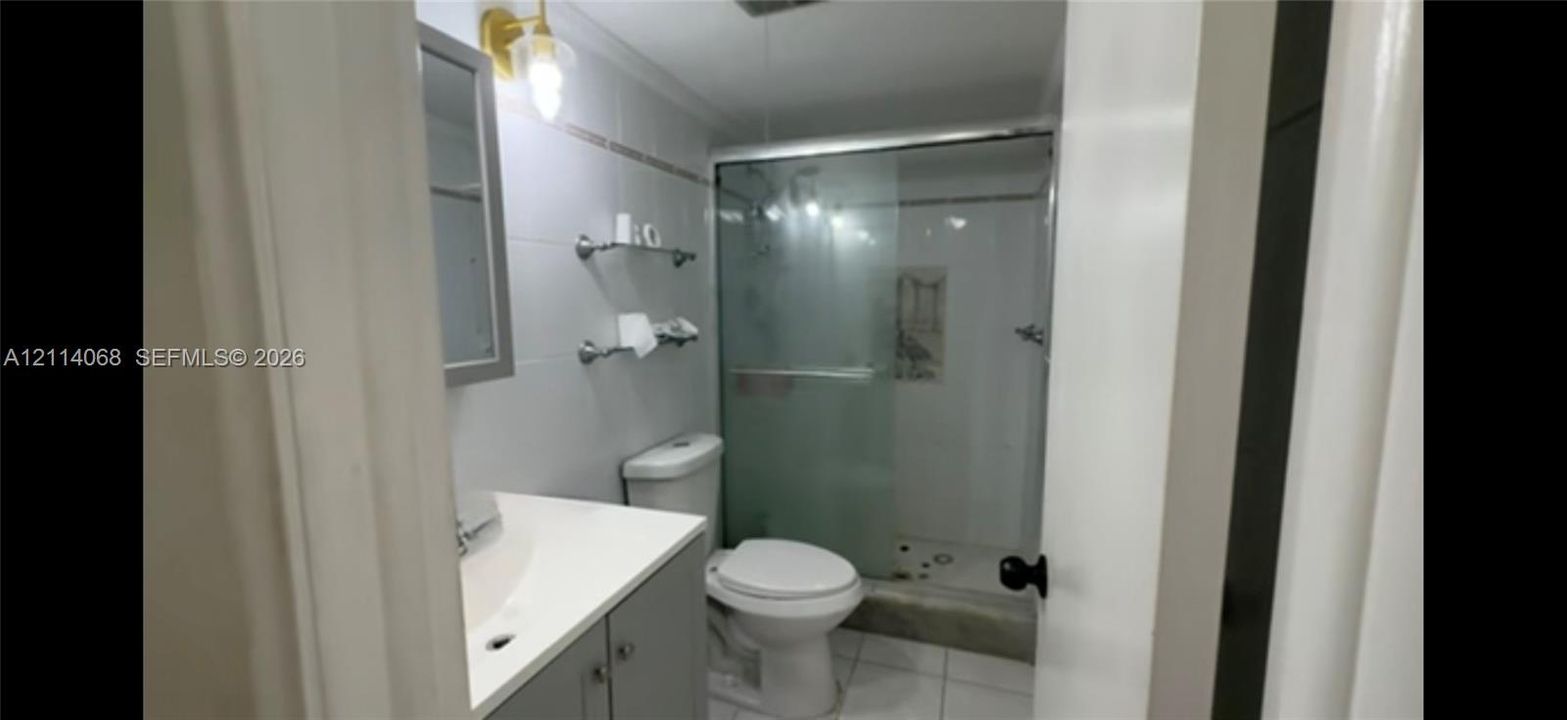 Bathroom featuring a vanity with a white countertop, wall-mounted metallic shelving, a shower enclosure with sliding glass doors, and light-toned tile flooring