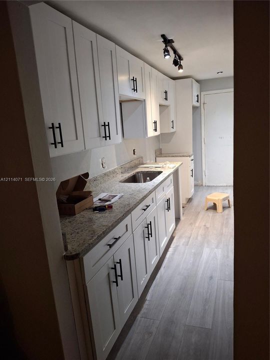 Kitchen featuring white shaker-style cabinetry with matte black hardware, stone-finish countertops, stainless steel undermount sink, wood-finish flooring, and track lighting
