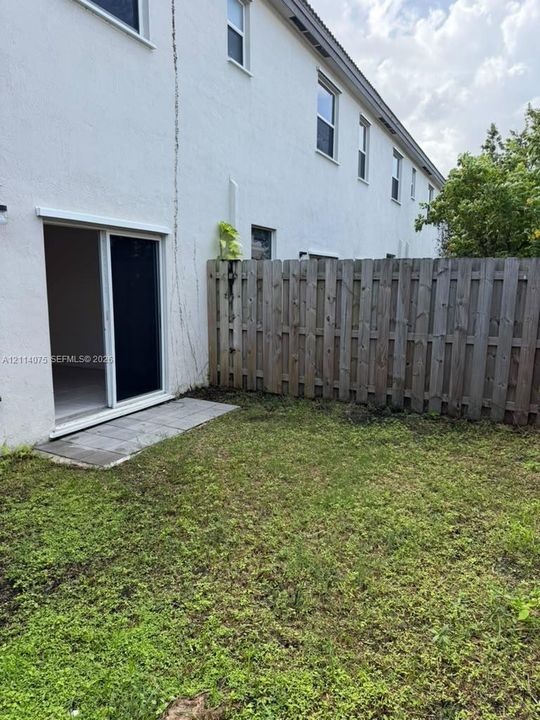 Exterior space featuring a grassy lawn, a vertical wood privacy fence, and a sliding glass door with a concrete patio landing