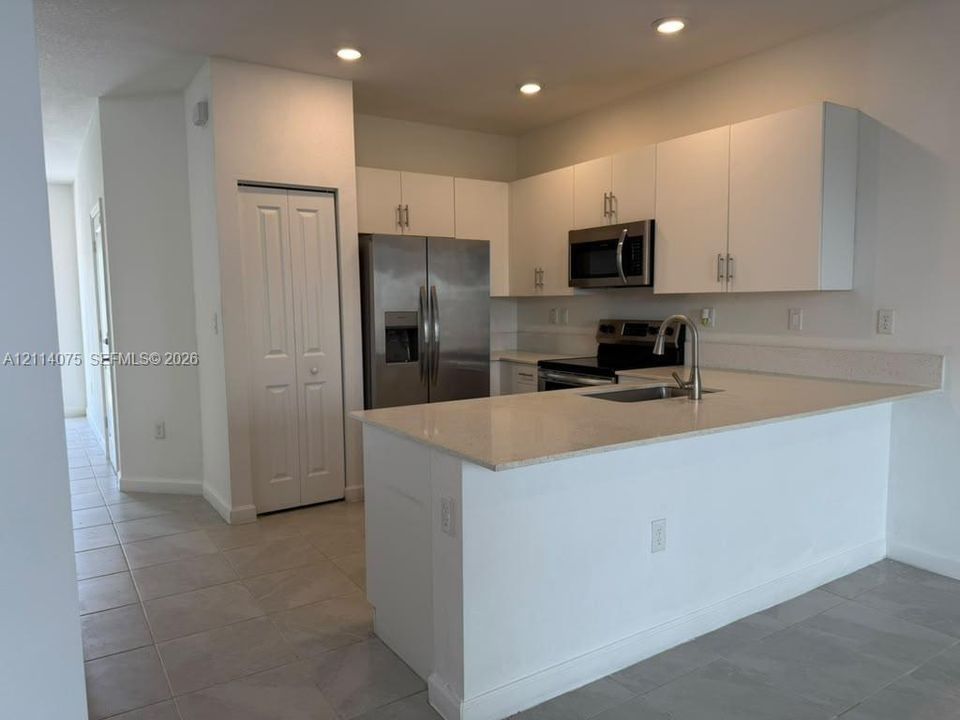 Kitchen featuring white flat-panel cabinetry, stone countertops, stainless steel appliances, a peninsula with an undermount sink, and recessed lighting
