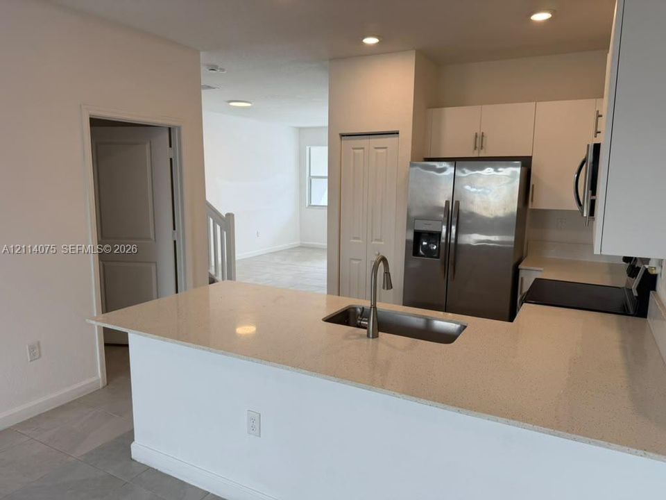 Kitchen featuring a stone-surface peninsula, stainless steel refrigerator, undermount sink with a gooseneck faucet, white cabinetry, and recessed lighting