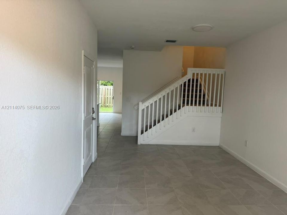 Interior space featuring large-format tile flooring, a painted white staircase with vertical balusters, and a paneled interior door