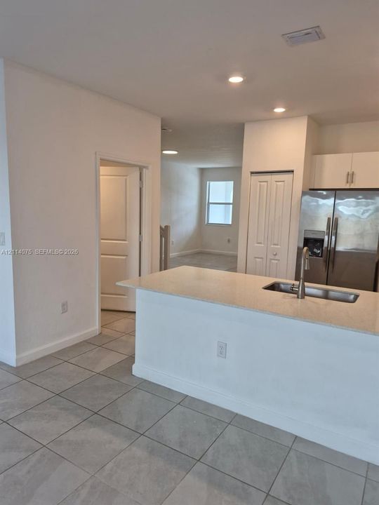 Kitchen featuring a stone-composite countertop island, stainless steel sink with a high-arch pull-down faucet, stainless steel refrigerator, and ceramic tile flooring