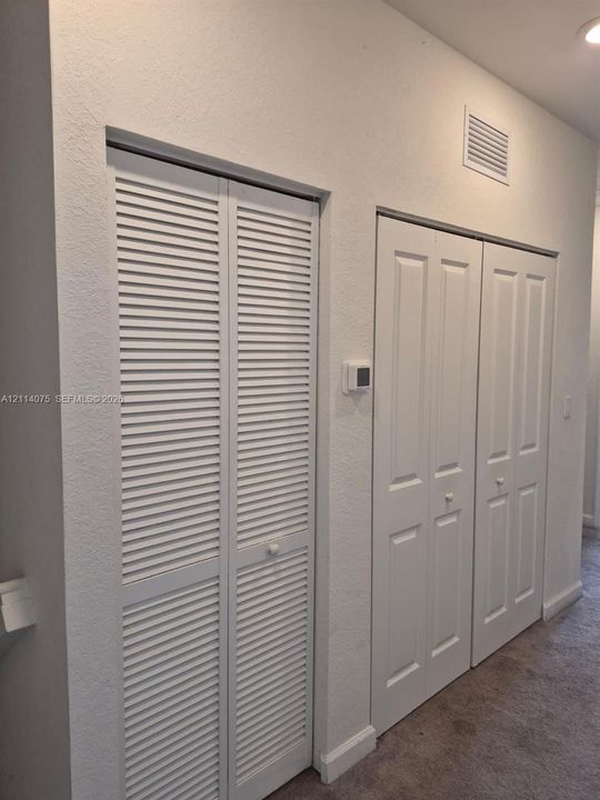 Wall-mounted thermostat featuring louvered bi-fold closet doors and dual-panel interior closet doors