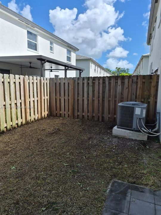 Rear exterior space featuring a privacy wood fence, covered patio area with ceiling fans, and an exterior heating and cooling unit on a concrete pad