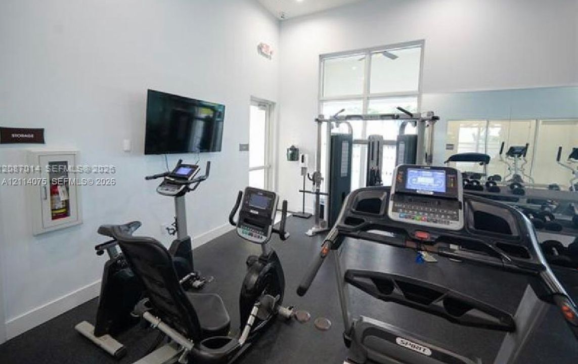 Fitness center featuring rubber flooring, large wall-mounted mirrors, high ceilings with clerestory windows, and a wall-mounted television
