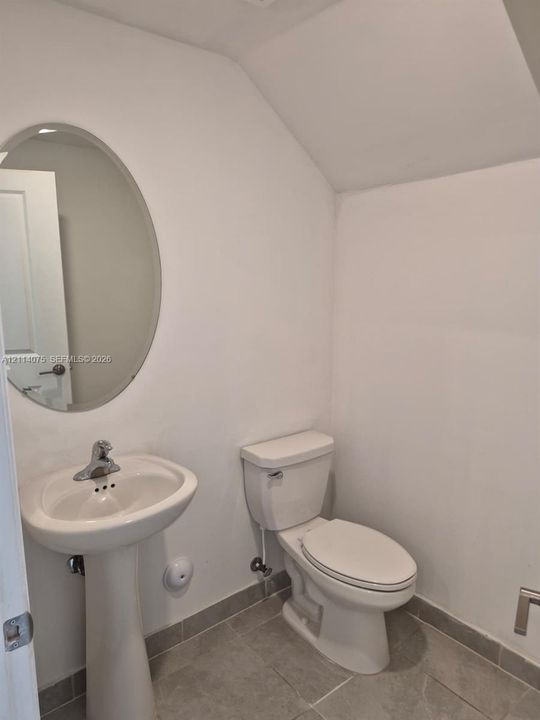 Oval wall-mounted mirror, white ceramic pedestal sink with chrome faucet, porcelain toilet, and neutral tile flooring