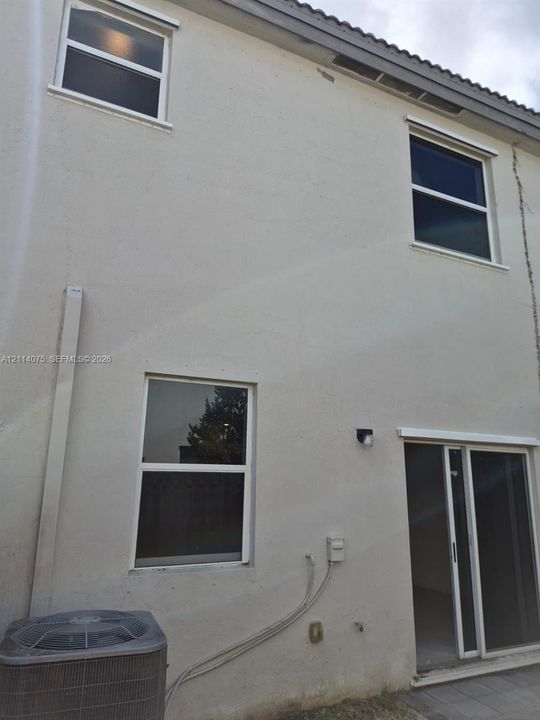 Two-story stucco exterior featuring single-hung windows, sliding glass door, and exterior wall-mounted light fixture