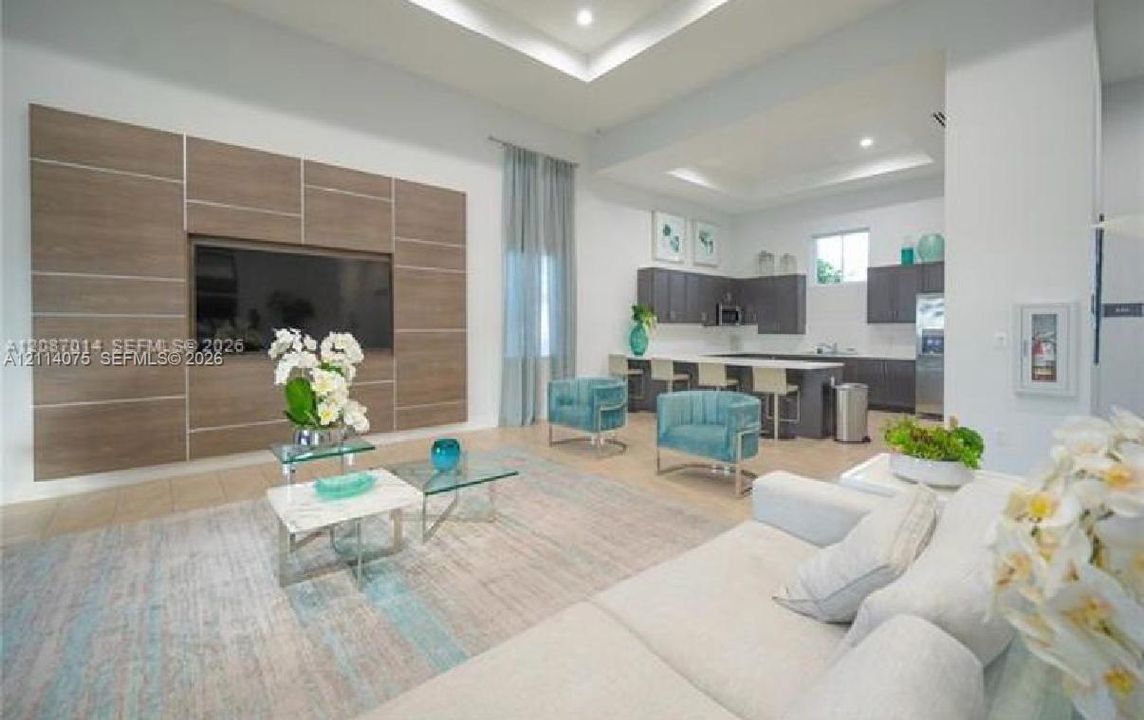 Tray ceiling with recessed lighting, custom wood-finish media wall, large-format tile flooring, kitchen island with bar seating, and dark-toned cabinetry