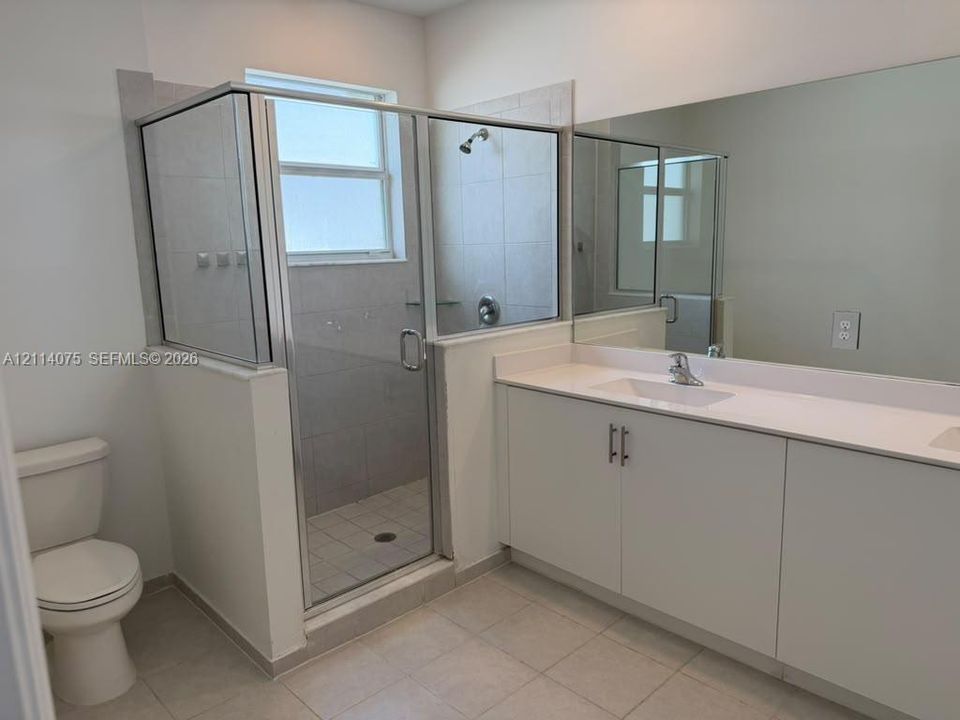 Bathroom featuring a walk-in shower with glass enclosure, vanity with solid-surface countertop, full-width wall mirror, and tile flooring