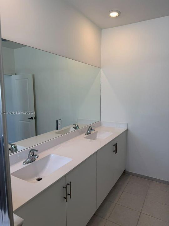 Dual-sink vanity with a solid-surface countertop, flat-panel cabinetry, brushed metal hardware, and a large-format vanity mirror