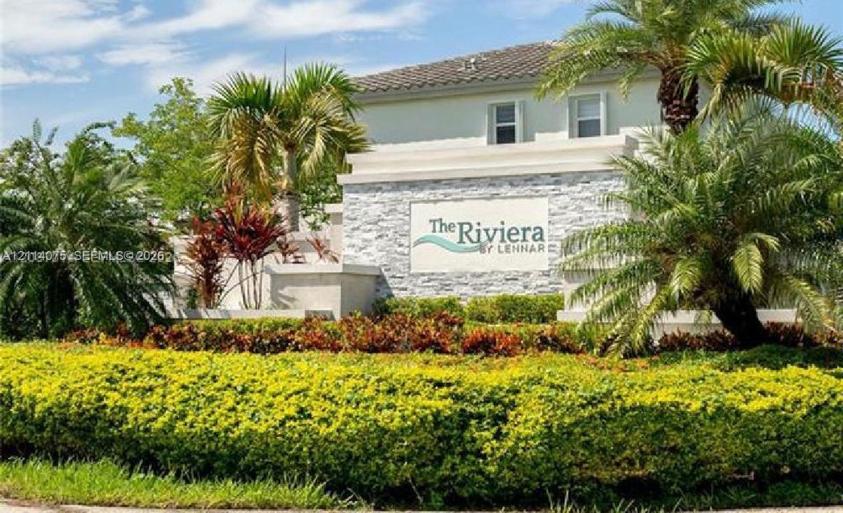 Community monument signage featuring stacked stone veneer, tiered architectural concrete walls, and mature tropical landscaping