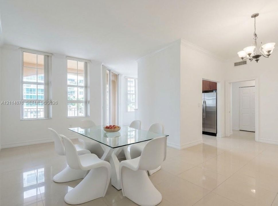 Bright open living area featuring neutral tile flooring, multi-pane windows, crown molding, and a multi-arm chandelier