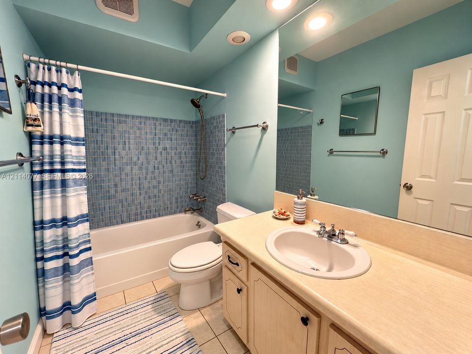Bathroom featuring a bathtub with blue mosaic tile surround, built-in vanity with a solid surface countertop, integrated oval sink, and large wall-mounted mirror