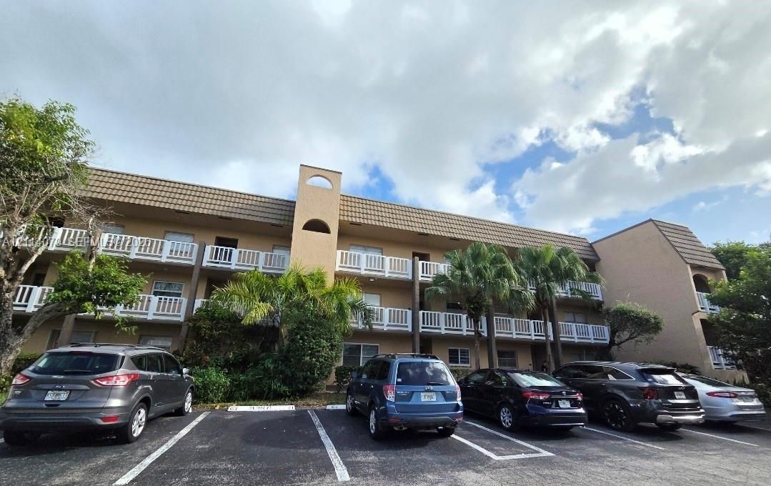 Multi-story building exterior featuring a textured stucco facade, Mansard-style roofline, and white balcony railings