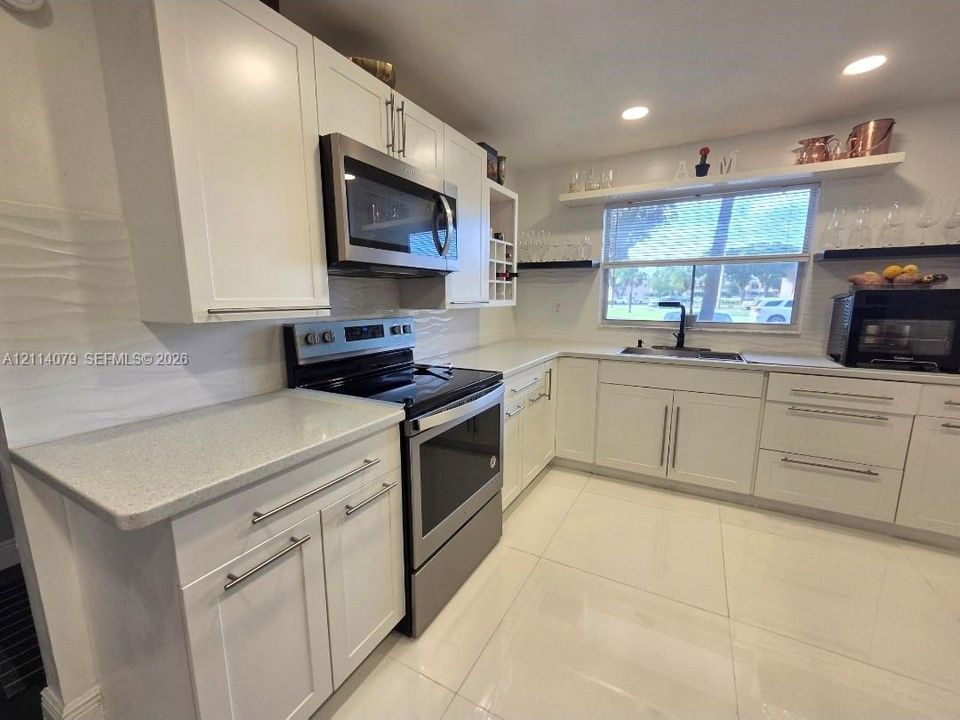 Kitchen featuring white cabinetry, solid-surface countertops, stainless steel appliances, a matte black faucet, and large-format tile flooring