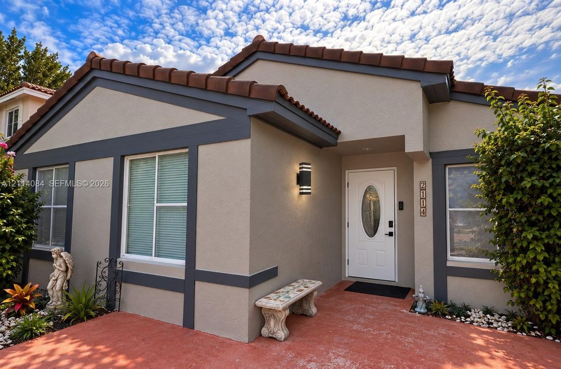 Stucco exterior featuring dark-toned trim, a terracotta tile roof, a central entryway with an oval-glass paneled door, and modern cylinder-style wall-mounted lighting