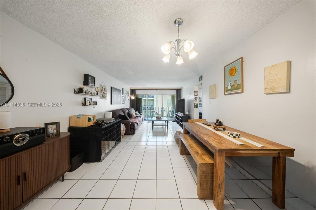 Open-concept interior featuring large-format ceramic tile flooring, a multi-arm polished metal chandelier, and a sliding glass door providing access to a private balcony
