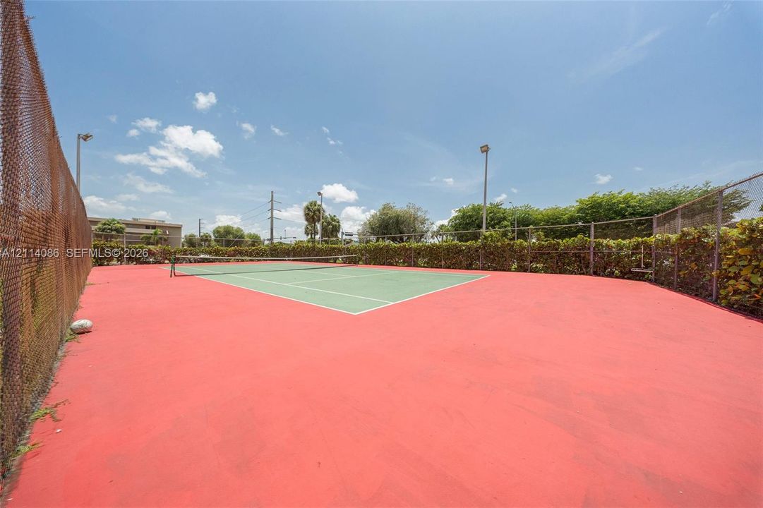 Private tennis court featuring a hard surface, perimeter chain-link fencing, and integrated lighting poles