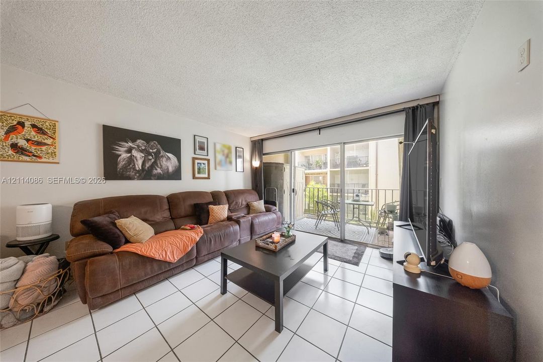 Living area featuring white ceramic tile flooring and sliding glass doors with access to an exterior balcony
