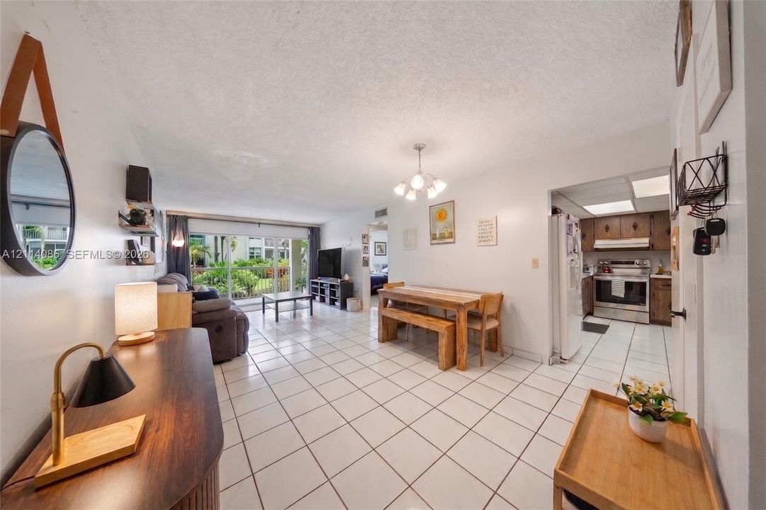Open floor plan featuring large format ceramic tile flooring, multi-arm chandelier lighting, sliding glass balcony doors, and kitchen cabinetry with integrated appliance housing