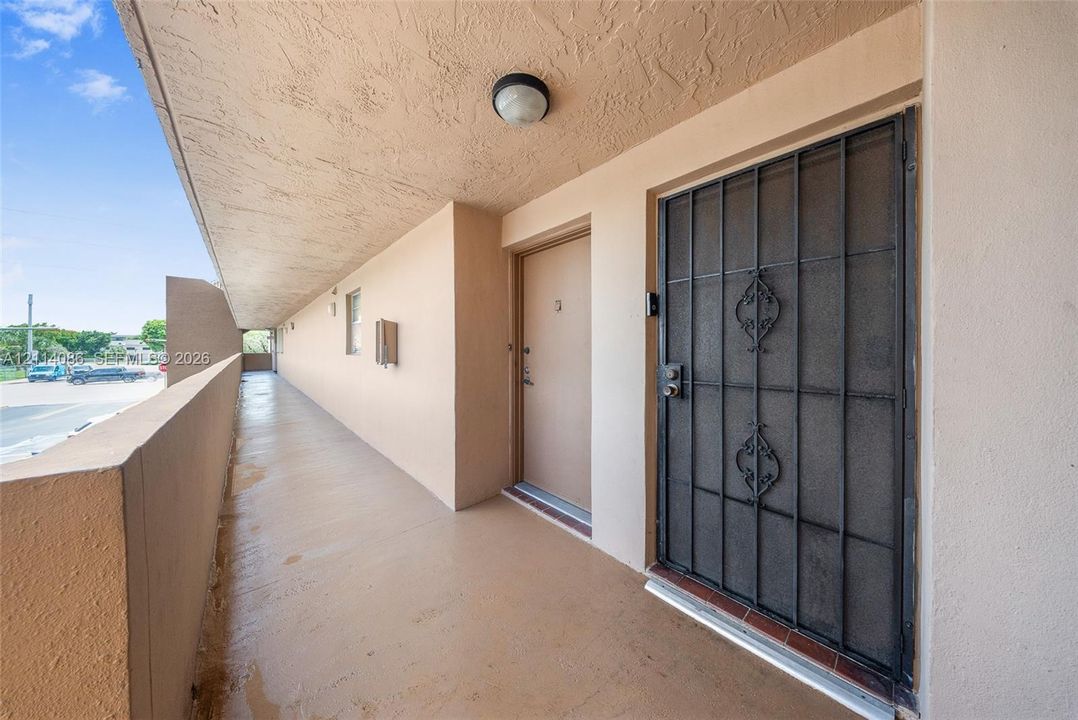 Covered exterior walkway featuring a protective metal security door, recessed ceiling lighting, and solid surface flooring