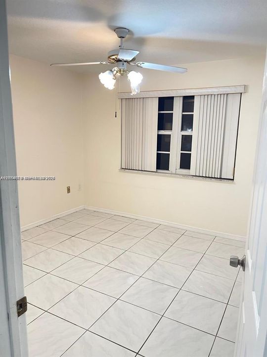 Neutral-toned interior featuring large-format tile flooring, a multi-blade ceiling fan with integrated lighting, and vertical window blinds