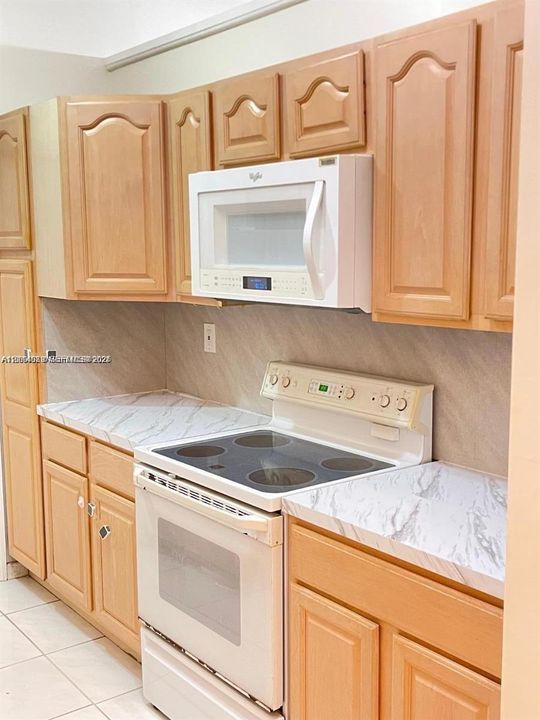 Kitchen featuring natural wood-finish cabinetry, stone-patterned laminate countertops, tile backsplash, and white appliance package