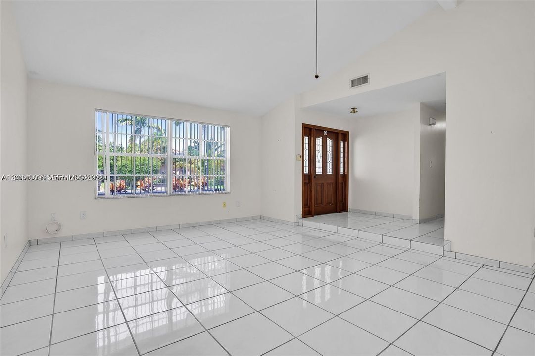 Vaulted ceilings, white ceramic tile flooring, large-format window with security bars, and a wooden entry door featuring glass inserts
