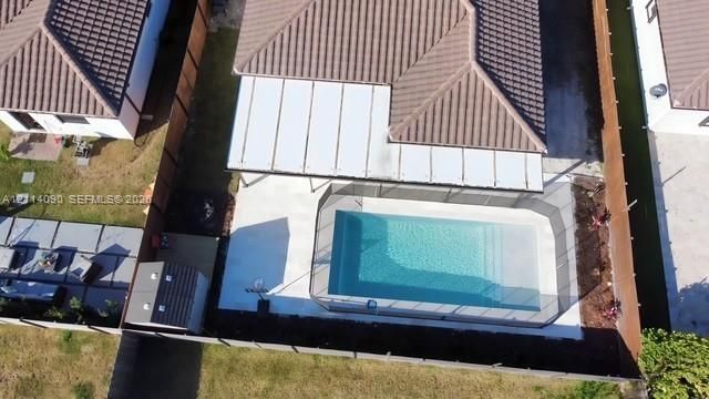 Aerial perspective of a backyard featuring a swimming pool with a surrounding mesh safety fence, a concrete patio, a covered pergola, and a storage shed, all enclosed by wood-panel fencing