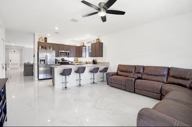 Open concept interior featuring polished tile flooring, dark wood-finish cabinetry, stainless steel appliances, a peninsula with stone-finish countertops, and a modern ceiling fan