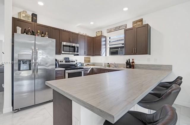 Kitchen featuring dark wood cabinetry, stainless steel appliances, wood-finish breakfast bar, and light-toned tile flooring