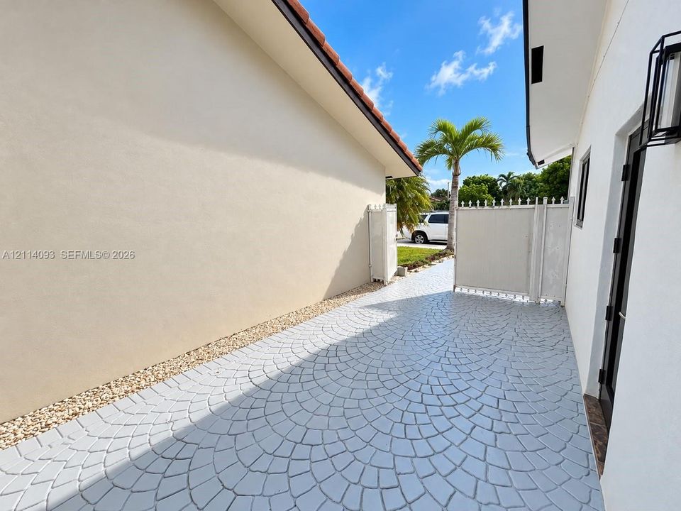 Side exterior featuring stamped concrete patio, light-colored stucco siding, gravel ground cover, and a white privacy gate
