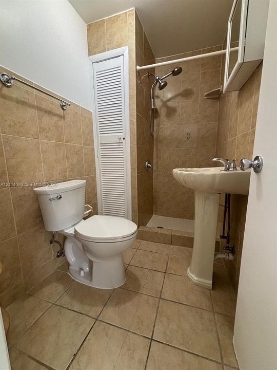 Bathroom featuring a pedestal sink, a walk-in shower with tile surround, full-wall tile backsplash, and built-in closet with louvered doors