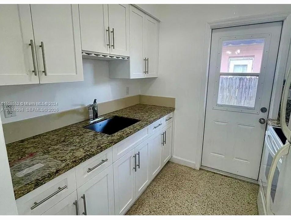 White cabinetry with integrated wine storage, stone-finish countertops, black inset sink with chrome faucet, and exterior access door with glass panel