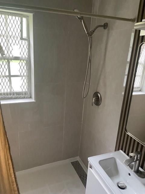 Bathroom featuring a tiled shower enclosure with a handheld showerhead, a single-basin vanity with a chrome faucet, and a window with security screening
