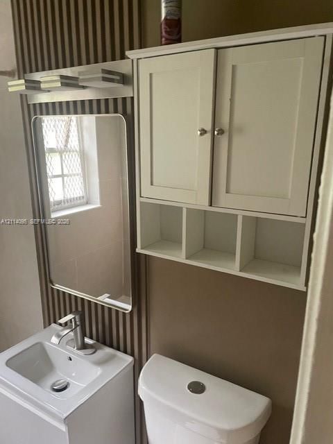 Bathroom vanity featuring a rectangular basin and single-handle faucet, wall-mounted rectangular mirror, tiered linear light fixture, white dual-door wall cabinet with open shelving, and porcelain toilet