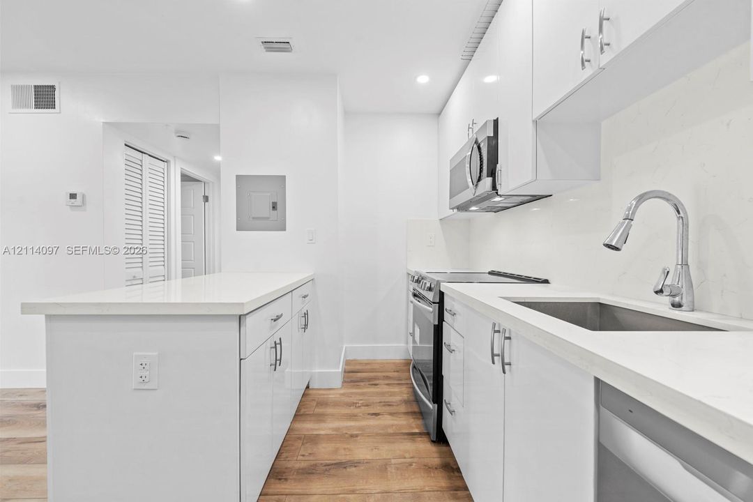 Kitchen featuring high-gloss white cabinetry, quartz countertops, a stainless steel under-mount sink with a gooseneck faucet, stainless steel appliances, and wood-finish flooring