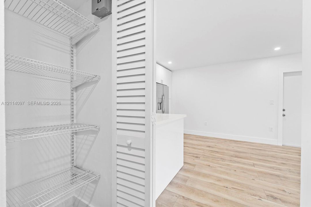 Pantry featuring white louvered doors and adjustable wire shelving, offset by wood-finish flooring, recessed lighting, and white cabinetry