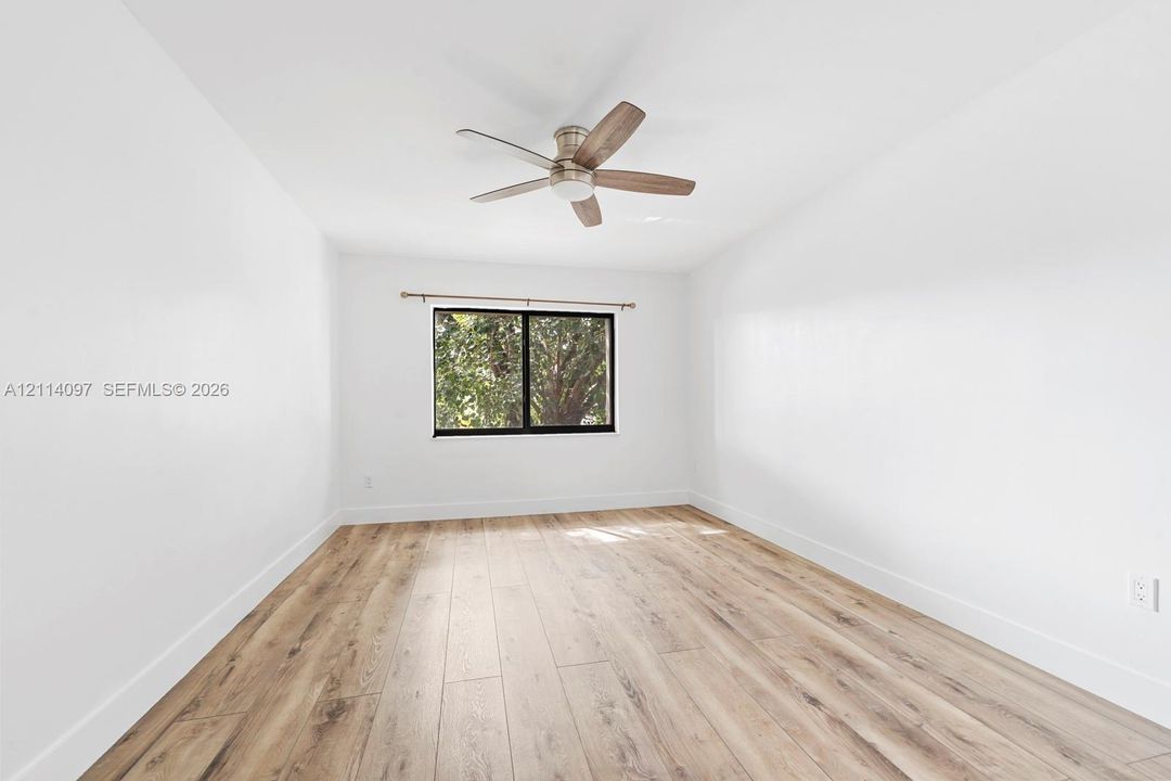 Neutral interior featuring wood-finish flooring, a ceiling fan with integrated lighting, and a window with a dark frame