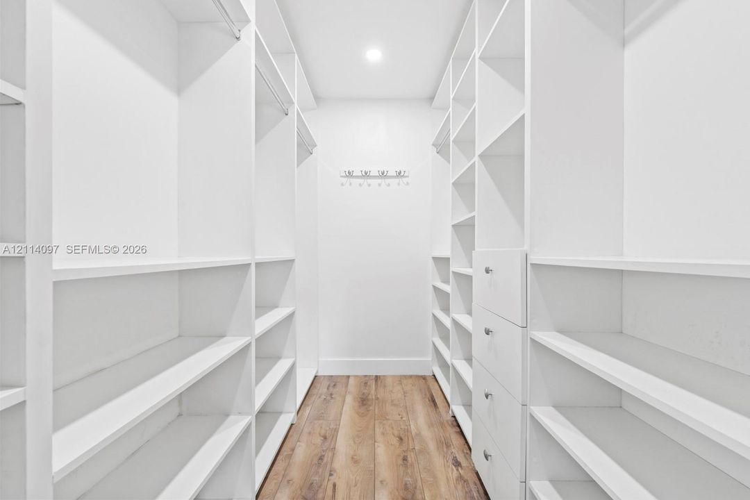 Walk-in closet featuring white built-in shelving, integrated garment rods, custom drawer storage, and wood-finish flooring